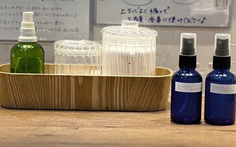 木のトレーに、緑のスプレーボトルと綿棒・コットンを入れたガラスの容器。手前に青いスプレーボトルが2本