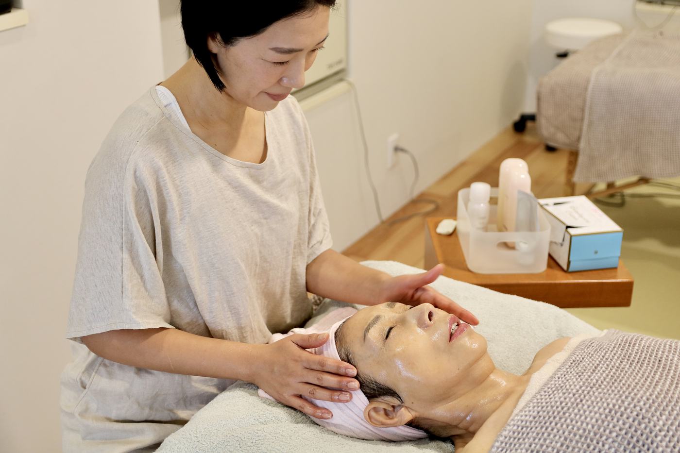 横になった人の顔に、スタッフが両手をそえている