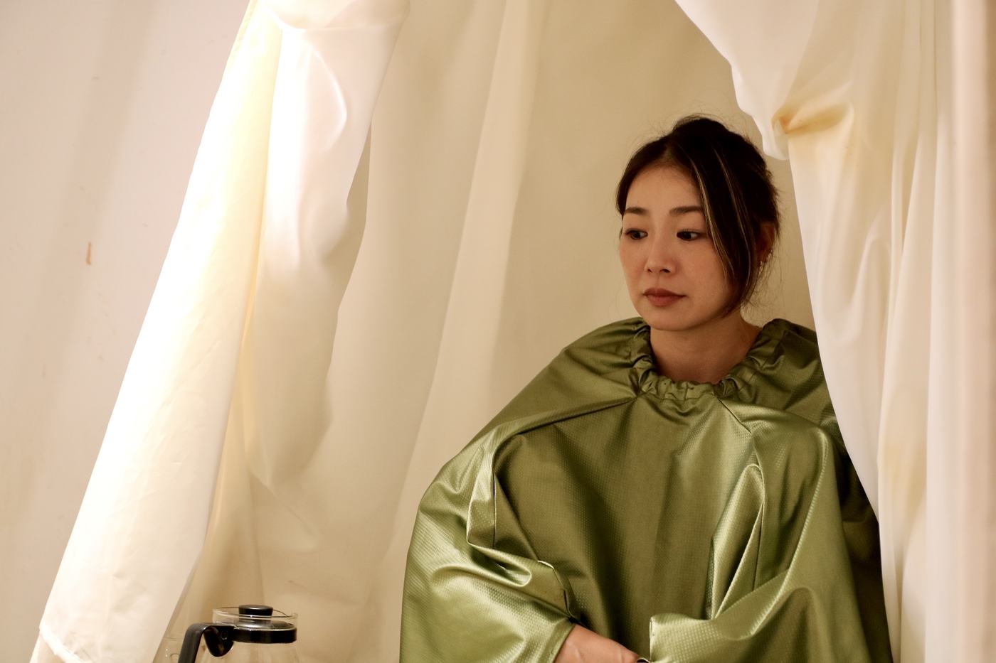 カーテンの中で、よもぎ蒸しのガウンを着て座っている