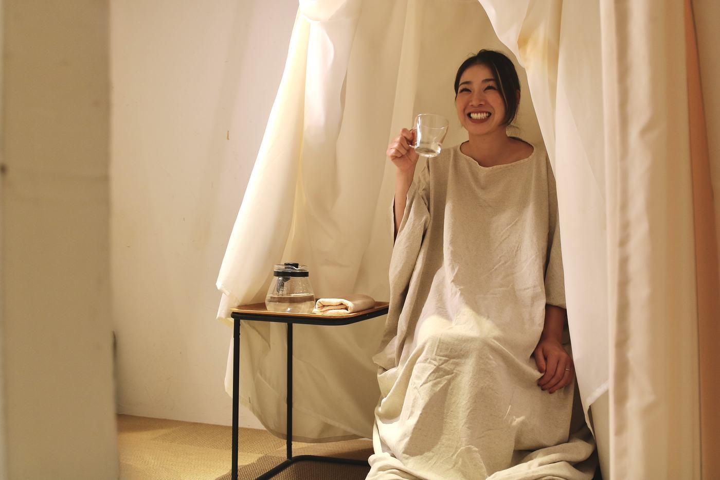 よもぎ蒸しのガウンを着て、グラスを手に笑っている