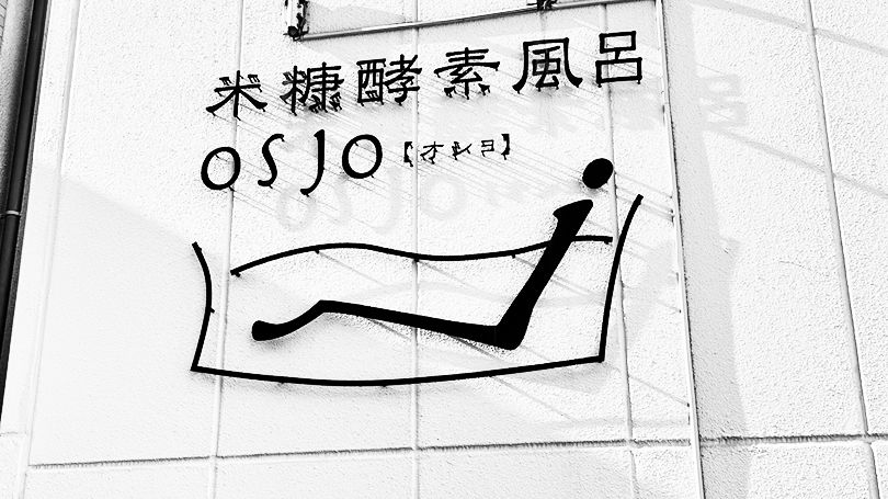 壁面のロゴサイン。「米糠酵素風呂 OSJO【オショ】」の文字と、浴槽に寝そべる人のマーク